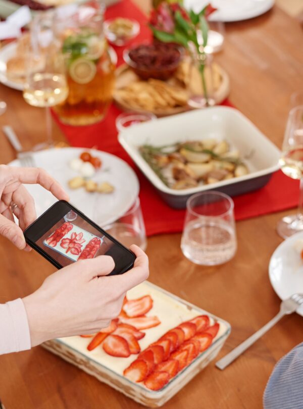 A person captures a photo of strawberry tiramisu at a lively dinner gathering.